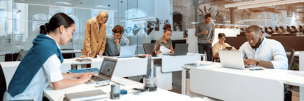 imagem de pessoas sentadas ao computador e outras em pé em um ambiente corporativo.